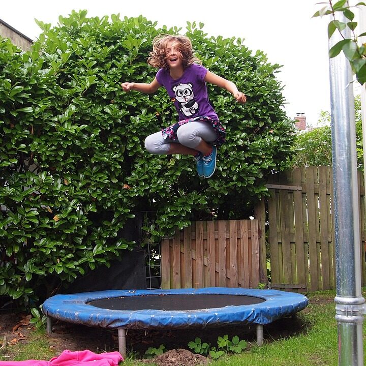 Flicka som hoppar på en studsmatta i en trädgård.